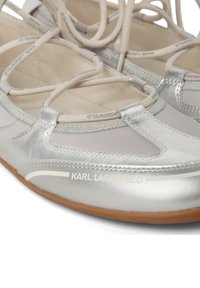 Ballerines en argent métallisé avec un design à lacets. Présentent une texture lisse, des accents gris subtils et une semelle en caoutchouc beige. Marque visible.