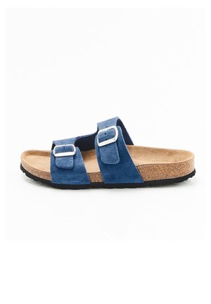 Sandale en daim bleu avec deux boucles argentées réglables, semelle intérieure en liège et semelle noire texturée, vue de côté.
