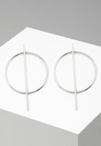Boucles d'oreilles en argent présentant un design épuré avec des anneaux circulaires et une barre verticale droite qui croise chaque cercle.