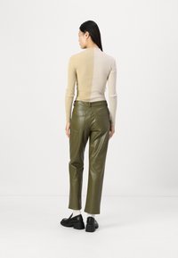 Haut beige côtelé avec un col montant, associé à un pantalon en simili cuir vert olive. Des chaussures noires à semelles épaisses complètent le look.