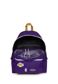 Mochila morada de tela, con detalles en blanco, cierre de cremallera y logotipos de la NBA y Eastpak en el frente. Bolsillo interior visible.