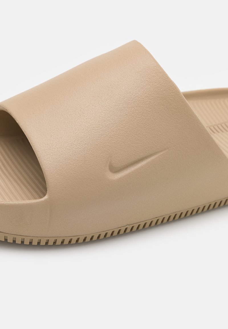 Sandale slide beige en plastique texturé avec un design à bout ouvert. Équipée d'un petit logo Nike en relief et d'une semelle nervurée pour une meilleure traction.