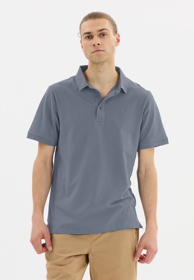 Ljusgrå kortärmad polo-shirt med krage, med en liten logotyp på bröstet och en avslappnad passform. Slät, mjuk tygtextur.