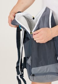 Mochila de color azul marino con acentos grises, que cuenta con una gran cremallera, tejido texturizado y correas ajustables. El interior está forrado con un material blanco.