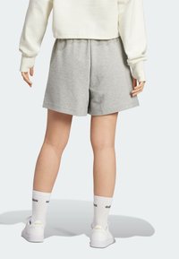 Grå texturerade shorts med elastisk midja, kombinerade med vita strumpor och sneakers, sedda bakifrån mot en ljus bakgrund.