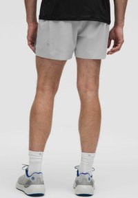 Herren graue Sportshorts mit einem perforierten Design. Das Model trägt weiße Socken und graue Sneakers mit blauen Akzenten.