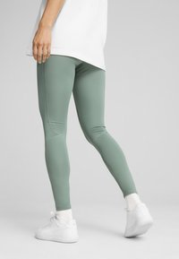 Lichtgroene leggings van rekbare, gladde stof. Heeft een aansluitend ontwerp, contrasterende naden en is gecombineerd met witte sneakers.