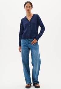Marinblå kofta med knappar och ribbat fåll och manschetter, med sex stora knappar. Kombinerad med ljusblå, löst sittande jeans.