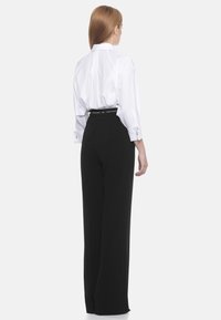 Camicia bianca oversize con bottoni e maniche arrotolate, abbinata a pantaloni larghi a vita alta neri con una cintura con marchio.