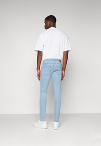 Jeans skinny azul claro de denim con una etiqueta trasera. Combinados con una camiseta blanca básica y zapatillas blancas.