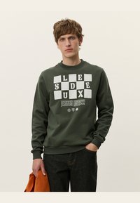 Sudadera de algodón verde con cuello redondo y mangas largas; presenta un diseño gráfico audaz en texto blanco en la parte frontal.