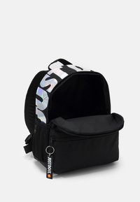 Mochila negra con una correa brillante e iridiscente que dice "SÓLO HAZLO", cierre con cremallera, bolsillo delantero y bolsillo lateral de malla para almacenamiento adicional.