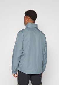 Let blå jakke med høj krave, elastiske manchetter og et enkelt design. Stoffet synes glat, med minimal detaljering og uden synlige mønstre.