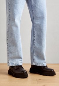 Chaussures en cuir noires avec une semelle épaisse et striée, assorties à un jean en denim bleu clair ample. Les chaussures présentent des bouts arrondis et un minimum de fixations.