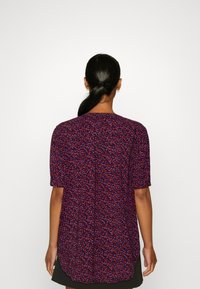 Blusa de manga corta en tejido azul marino, con un patrón floral multicolor, ligeramente más larga por detrás y cuello redondo.
