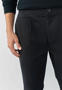 Fekete nadrág sima anyagból, rugalmas derékkal. Oldalzsebekkel és egyetlen gombos záródással az elején.