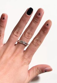 Nagelkonst som visar en hand med fem fingrar: tre hudfärgade naglar med svarta prickar, en helt svart nagel och en accentuerad silverring.