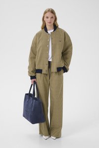 Jachetă supradimensionată galbenă cu carouri și accente bleumarin, asortată cu pantaloni cu același model și o geantă tote din piele întoarsă bleumarin. Cizme albe până la gleznă.