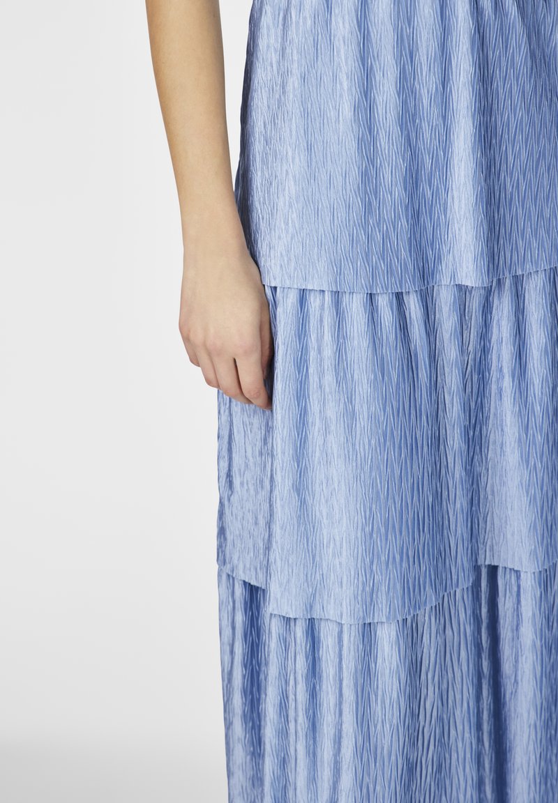 Jasnoniebieska sukienka warstwowa z fakturowanej tkaniny. Każda warstwa ma falisty wzór, a spódnica swobodnie opada do krawędzi.
