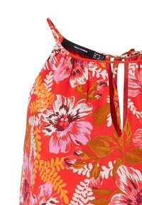 Blouse florale rouge ornée de grandes fleurs roses et blanches, de feuilles vertes, d'un décolleté en œillet et de fines bretelles. Confectionnée en tissu léger.