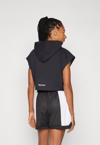 Juodas pasiriškos megztinis su kapišonu ir trumpomis rankovėmis, ant nugaros su Reebok logotipu. Suderinta su juodais ir baltais sportiniais šortais.