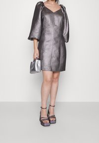 Metallinhohtoinen hopeanvärinen minimekko, jossa on puhvimaiset hihat ja teksturoitu pinta, V-aukko. Yhdistetty hopeanväriseen käsilaukkuun ja koristeellisiin korotettuihin korkokenkiin.