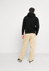 Sudadera negra con capucha de corte relajado, combinada con pantalones de pierna ancha en beige claro y zapatillas negras. Diseño simple, con un mínimo de detalles.