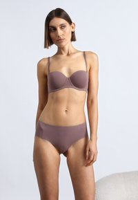 Lysebrun stropløs bh med glat tekstur og moderat polstring, kombineret med matchende hipstertrusser i samme farve og stof.