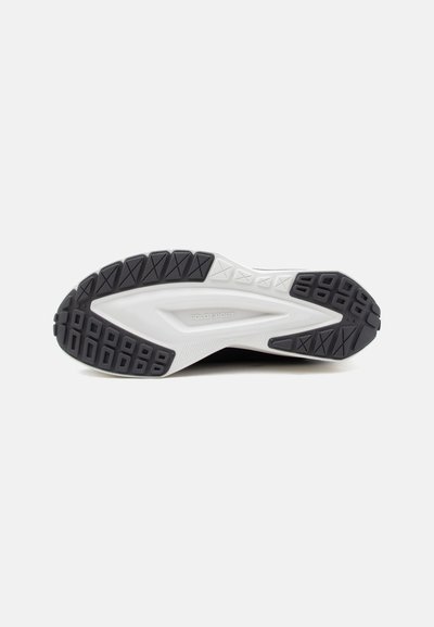 Semelle de chaussure avec une bande de roulement en caoutchouc noir et blanc, zones de grip texturées, et "Polo Sport" embossé au centre de la semelle intermédiaire blanche.