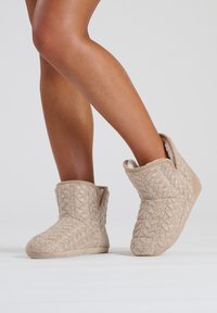 Botas de tobillo de punto beige con un patrón texturizado, forro suave y suela plana, que ofrecen comodidad con un ajuste ceñido.