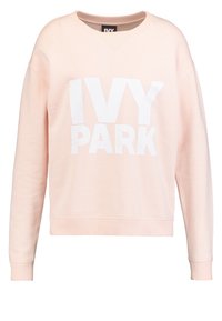 Sudadera de color rosa claro hecha de tela suave, con escote redondo, hombros caídos y gran logo blanco de "IVY PARK" en la parte frontal.