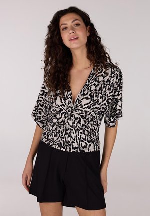 Leopardprint top met een diepe V-hals en korte mouwen, gecombineerd met zwarte shorts. De stof lijkt zacht en lichtjes gestructureerd.