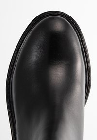 Bottine en cuir noir avec un bout arrondi, une texture lisse, des coutures contrastées et un talon bas et plat.