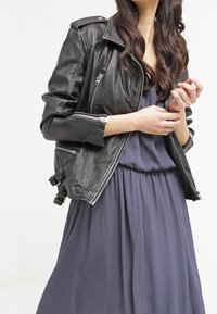 Svart skinnjacka med dragkedjefickor, axelklaffar och justerbara sidospännen, bärs över en flödande marinblå klänning.