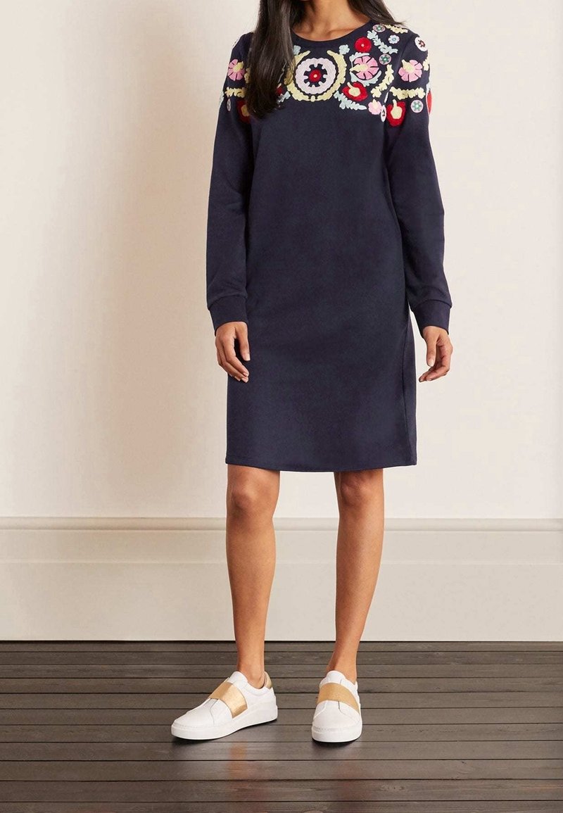 Abito navy a maniche lunghe con ricami floreali colorati sulle spalle. Abbinato a sneakers bianche con fasce beige. Tessuto con texture liscia.