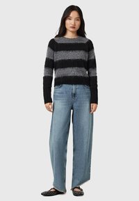 Maglione a righe in tonalità di nero e grigio, abbinato a jeans a gamba larga blu chiaro con orli grezzi e scarpe slip-on nere con borchie.