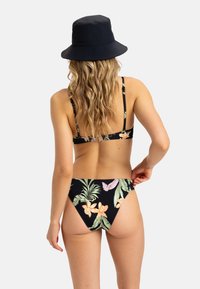 Svart bikiniöverkant och -underdel med en tropisk blommönster i rosa, orange och grönt. Modellen bär en svart bucket hat; bakvy visas.