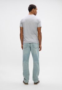 Grå kortærmet t-shirt parret med lyseblå denim jeans. Jeansene har et klassisk lige snit og detaljeret syning på baglommerne.