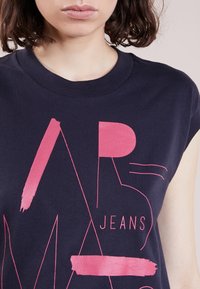 Námornícky modré tílko bez rukávů s odvážnými růžovými grafickými designy, včetně písmen a štětcových tahů. Měkká tkanina s uvolněným střihem.