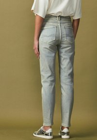 Jasnoniebieskie dżinsy z wysokim stanem o slim fit, z wyblakłą teksturą i tylnymi kieszeniami, w połączeniu z trampkami z srebrnymi akcentami.