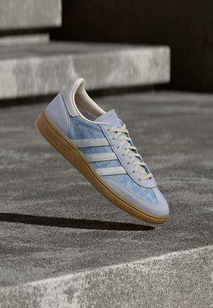 Lys blå joggesko med blomsterdekor, hvite striper og teksturerte grå semskede detaljer. Naturlig gummisåle. Lisser i kremfarget beige.