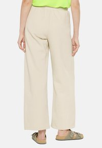 Beige wide-leg pants made of soft fabric, featuring an elastic waistband and rolled cuffs, paired with brown sandals on bare feet.