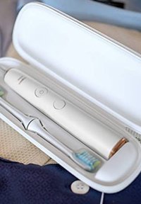 Spazzolino elettrico in una custodia bianca, con un manico beige liscio dotato di due pulsanti, accenti dorati e una testina dello spazzolino blu chiaro.