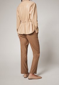 Chemise en simili cuir beige avec taille cintrée, pantalon marron ajusté et ballerines nudes. Texture lisse avec des détails de boutons sur les manches.