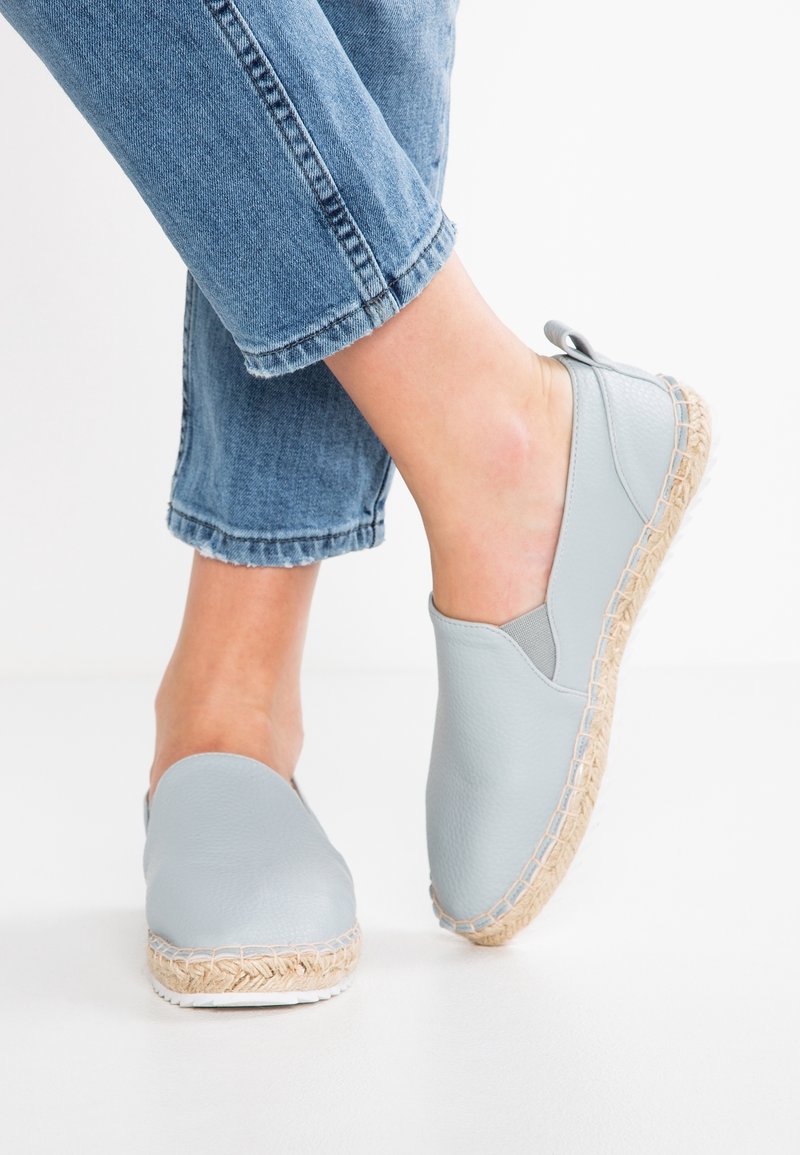 Baskets en cuir bleu clair à enfiler avec une semelle en corde de jute et un panneau latéral élastique, associées à un jean en denim retroussé.