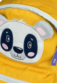 Zaino giallo con una faccia di panda in peluche, dotata di grandi occhi, dettagli ricamati e una texture liscia. Include un'etichetta viola.