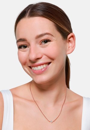Roze gouden ketting met een kleine, ronde hanger met een heldere edelsteen, gedragen door een persoon met lichte huid en bruin haar.