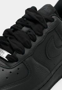 Sapata Nike Air Force 1 preta com couro texturizado, atacadores pretos grossos e etiqueta metálica "AF1" nos atacadores, em fundo branco.