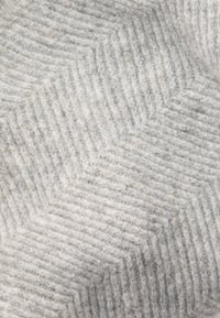 Tessuto di lana grigio con un motivo a spina di pesce caratterizzato da diverse trame e morbidezze. Il colore complessivo è grigio chiaro con accenti più scuri.