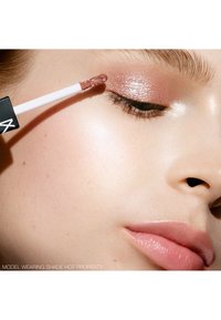 Gros plan d'une personne appliquant un fard à paupières liquide rose doré scintillant sur la paupière fermée avec un applicateur mousse.